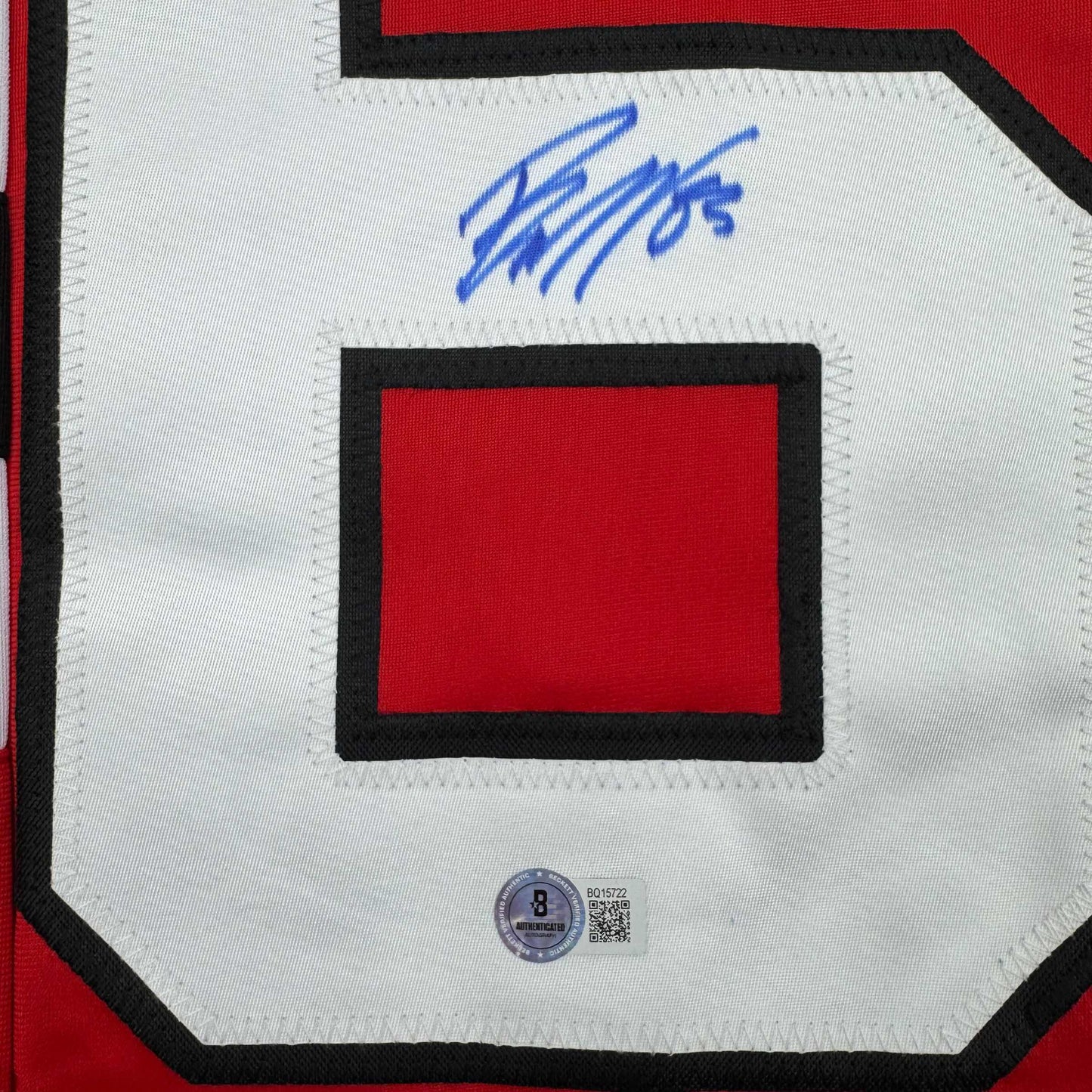 Close-up of red hockey jersey nameplate with black border and blue autograph above it, featuring Beckett authentication hologram.