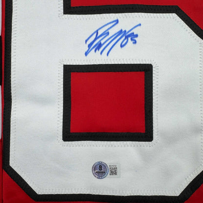 Close-up of red hockey jersey nameplate with black border and blue autograph above it, featuring Beckett authentication hologram.