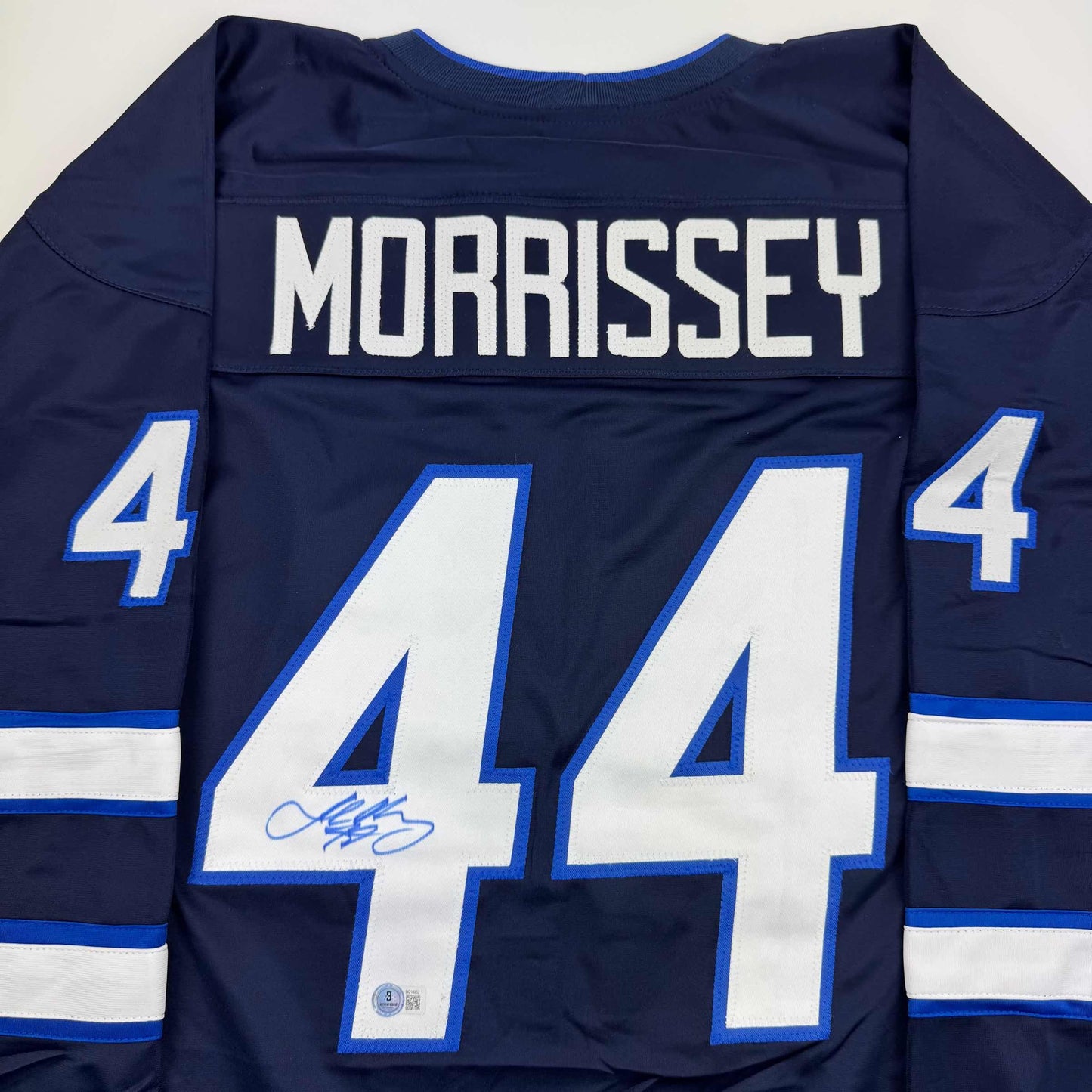 Back view of navy blue hockey jersey with white "MORRISSEY" nameplate and large white number 44 with blue outline, featuring blue and white striped sleeves and autograph on front of jersey.