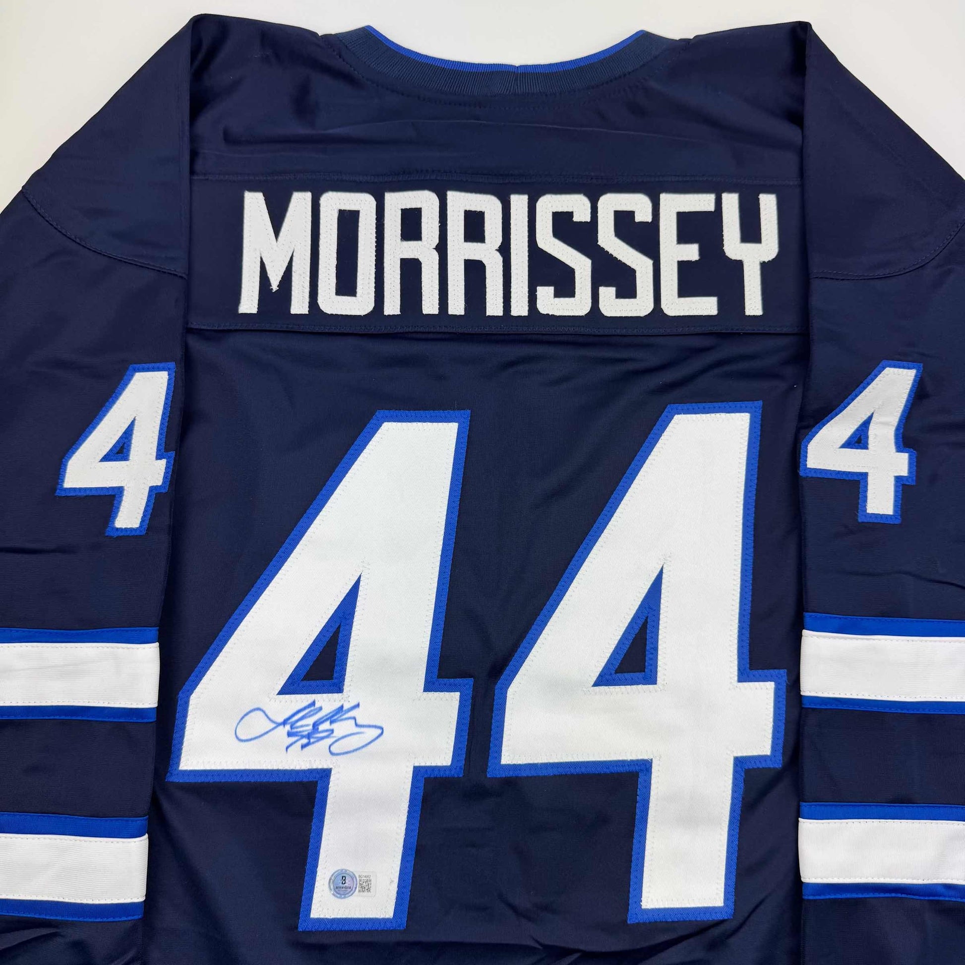 Back view of navy blue hockey jersey with white "MORRISSEY" nameplate and large white number 44 with blue outline, featuring blue and white striped sleeves and autograph on front of jersey.