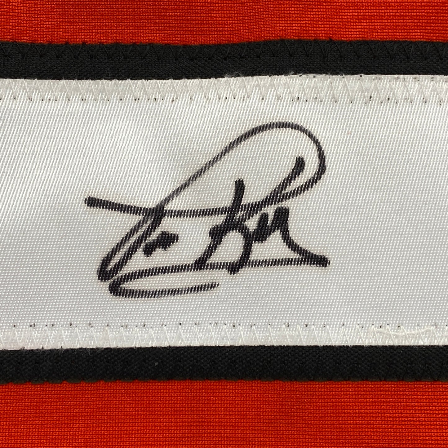 Close-up of black handwritten signature on white stripe of red, black, and white horizontal striped fabric.