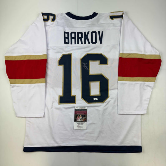 White hockey jersey with red and gold stripes displaying "BARKOV" and number 16, with JSA authentication certificate attached.