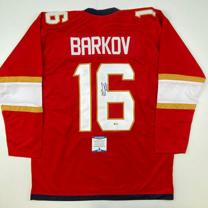 Red hockey jersey with white and gold trim displaying "BARKOV" and number 16, with visible signature and authentication certificate.