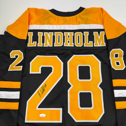 Back view of black hockey jersey with yellow and white stripes, large yellow number 28, "LINDHOLM" text, and autograph.