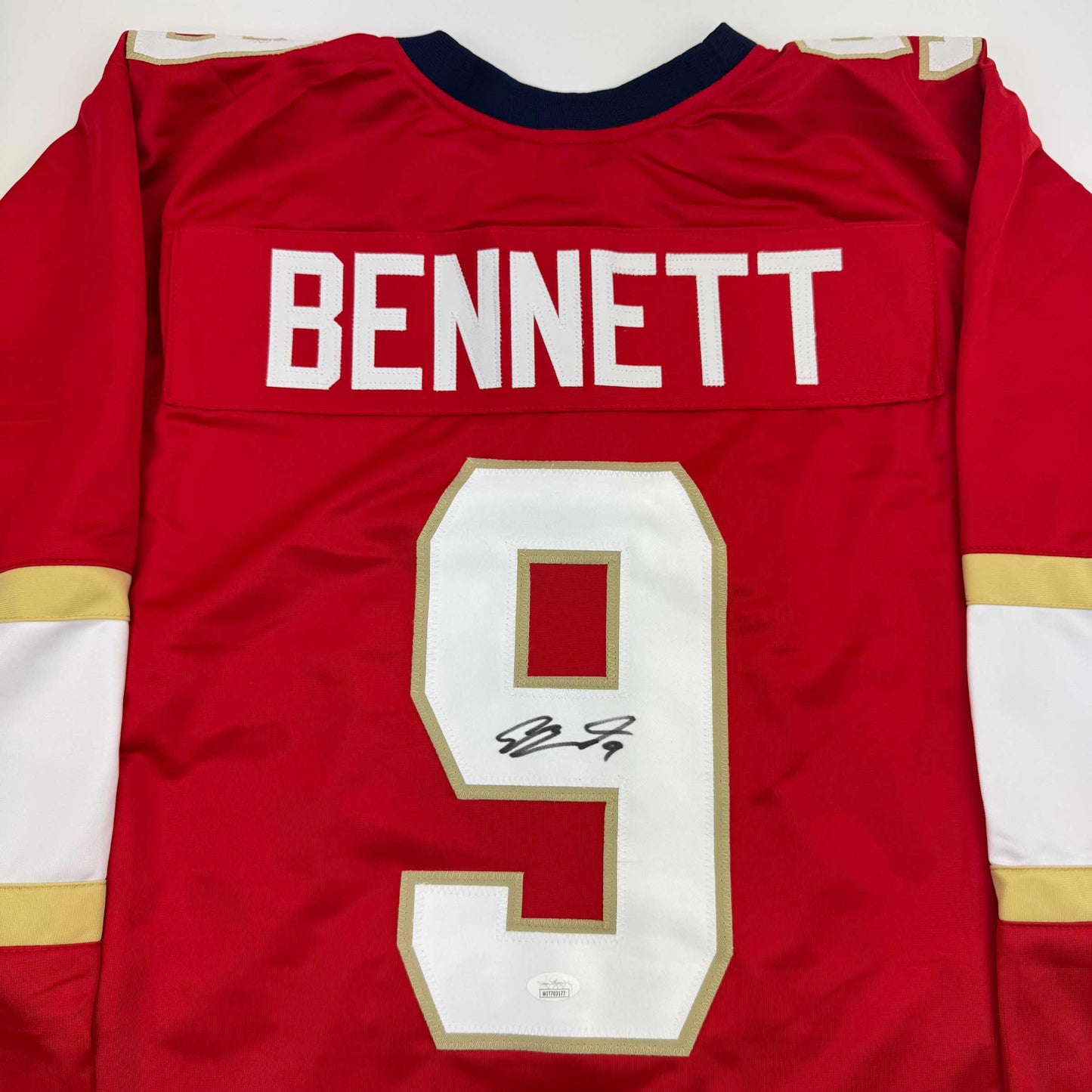Red hockey jersey with "BENNETT" nameplate and number 9 signed in black ink, displayed flat against white background.