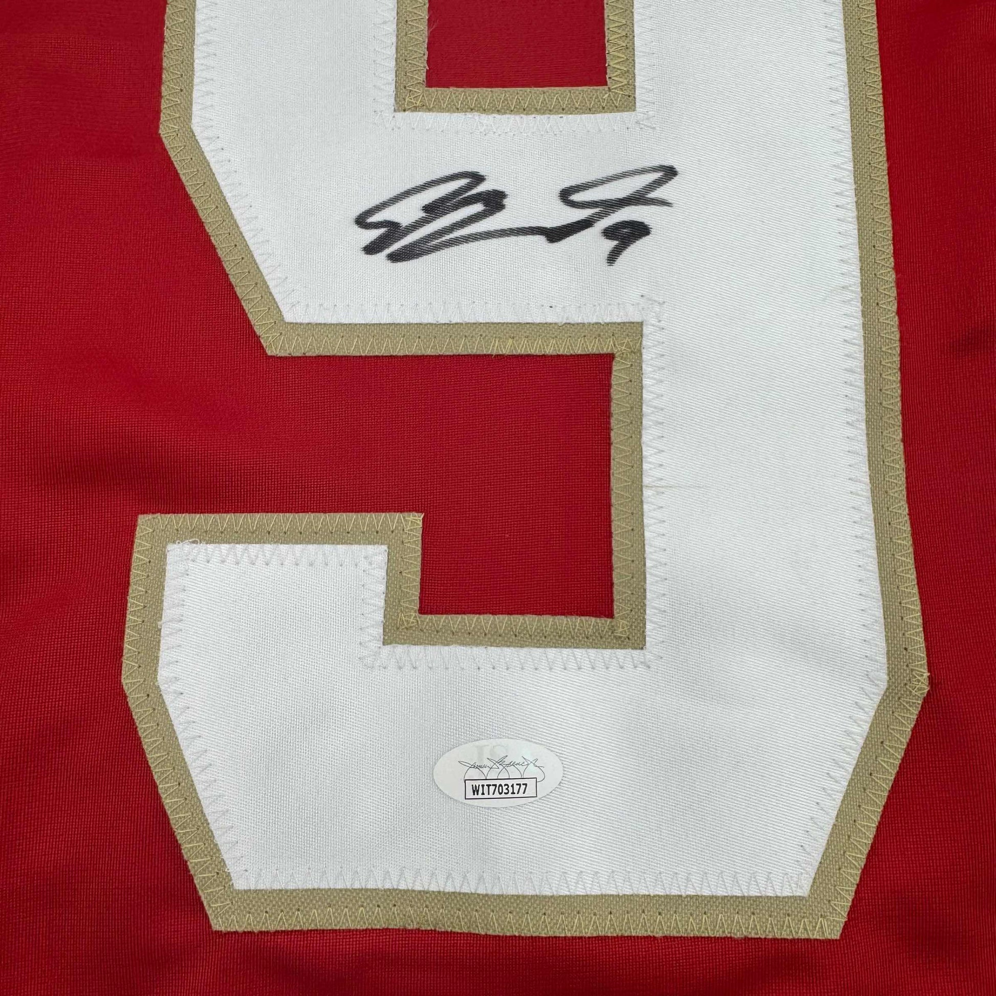 Close-up of signed red and white hockey jersey back showing autographed nameplate and authentication certificate.