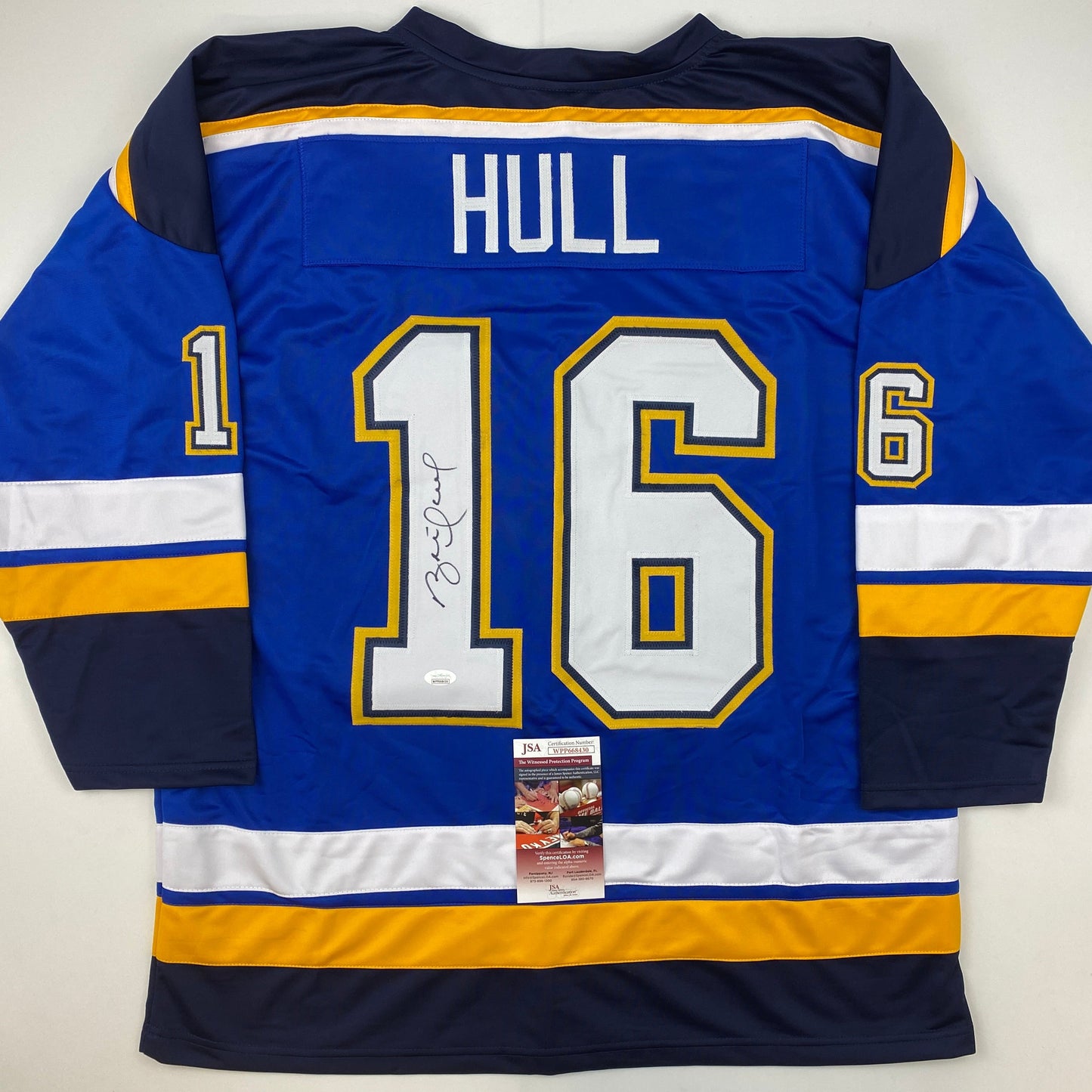 Reverse view of blue hockey jersey number 16 with "HULL" nameplate, signed in black ink, with JSA authentication sticker visible.