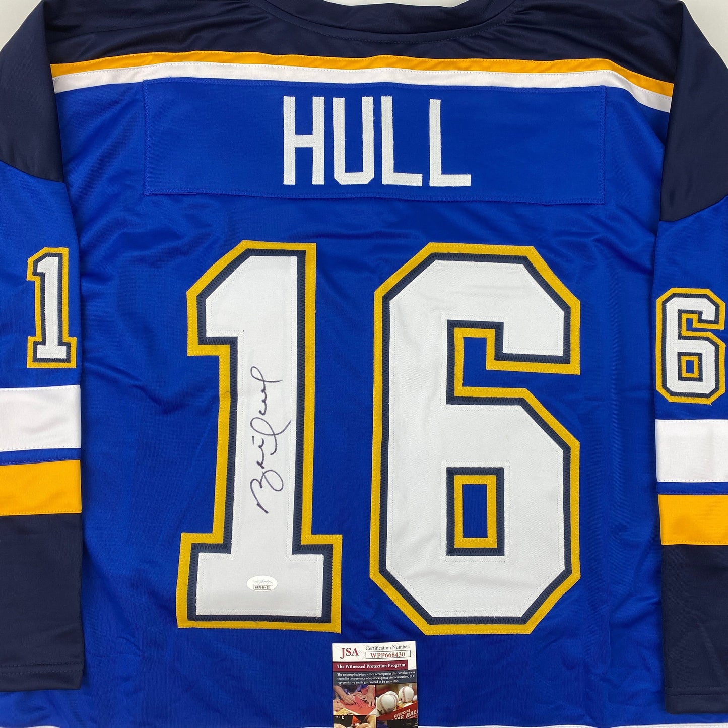 Blue hockey jersey with "HULL" across shoulders and large white "16" with signature, JSA certification visible at bottom.