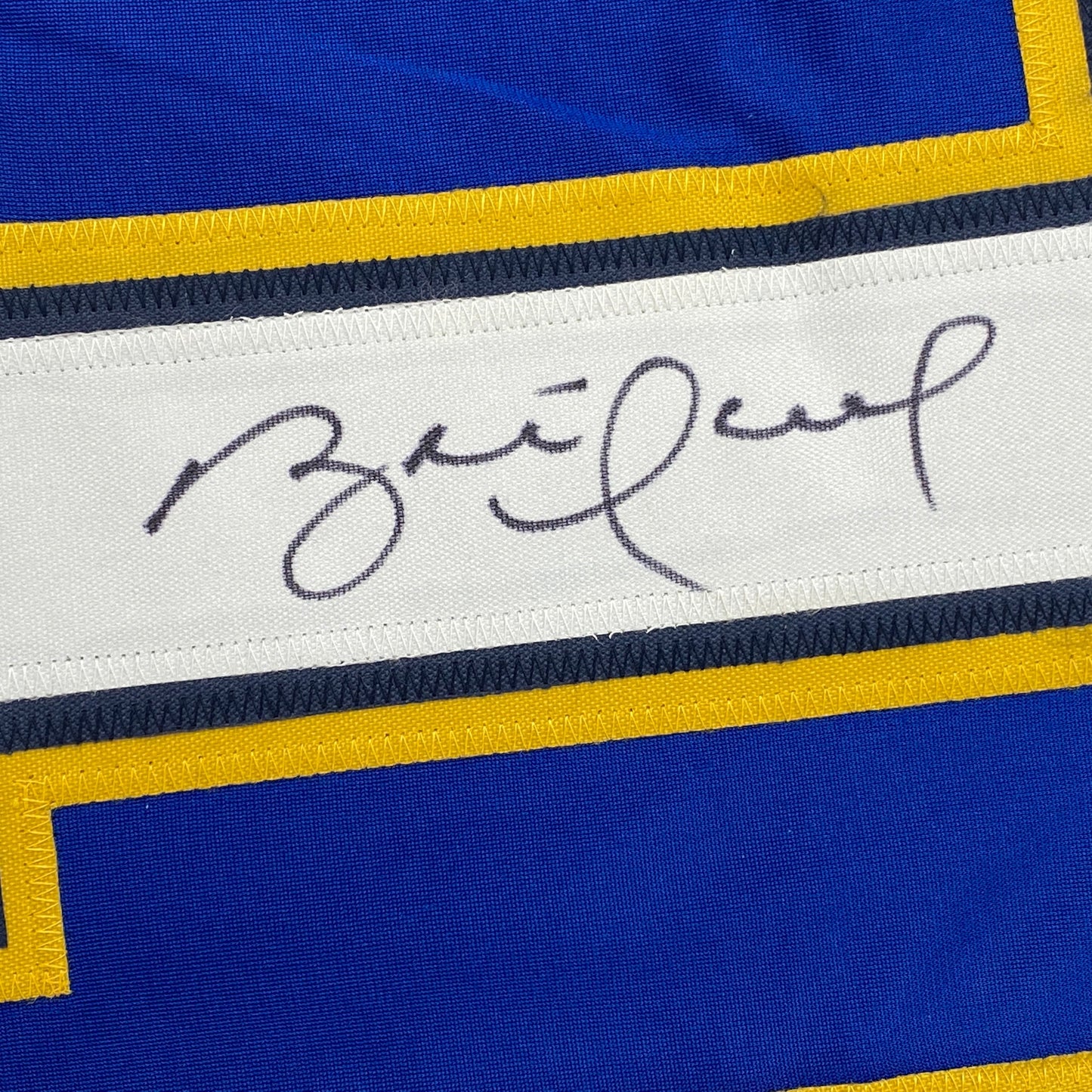 Close-up of handwritten signature on white stripe of blue and yellow striped hockey jersey.