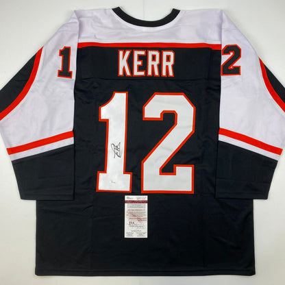 Back view of black Philadelphia Flyers hockey jersey number 12 with "KERR" nameplate and autograph, white and red trim, JSA authentication certificate visible.