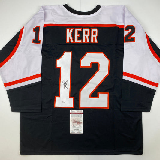 Back view of black Philadelphia Flyers hockey jersey number 12 with "KERR" nameplate and autograph, white and red trim, JSA authentication certificate visible.