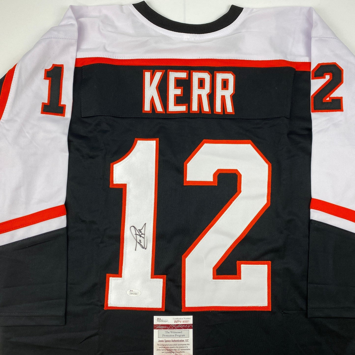 Back view of black hockey jersey with "KERR" and number 12 in red and white, signed in blue ink, with JSA authentication label at bottom.