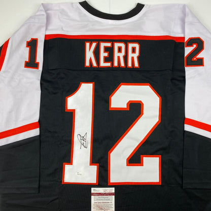 Back view of black hockey jersey with "KERR" and number 12 in red and white, signed in blue ink, with JSA authentication label at bottom.