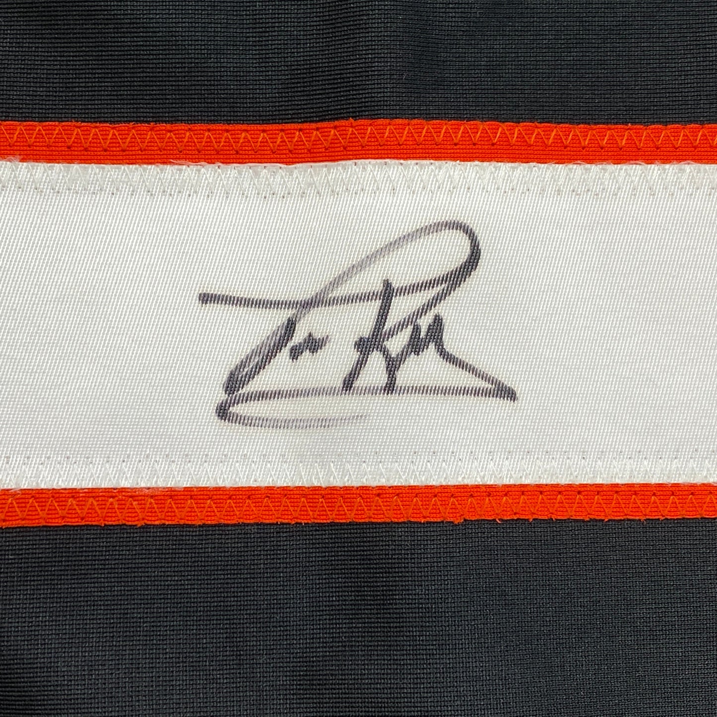 Close-up of handwritten signature on white stripe of black and orange striped hockey jersey.