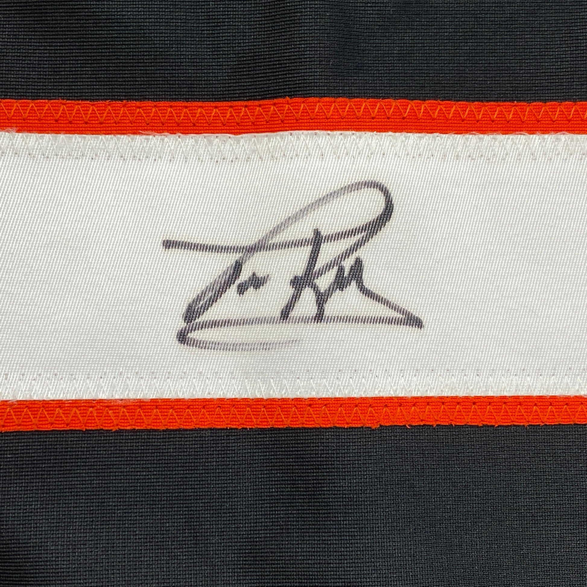 Close-up of handwritten signature on white stripe of black and orange striped hockey jersey.