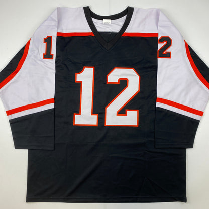 Black hockey jersey with red and white trim displaying number 12 in red and white on front, laid flat against white background.