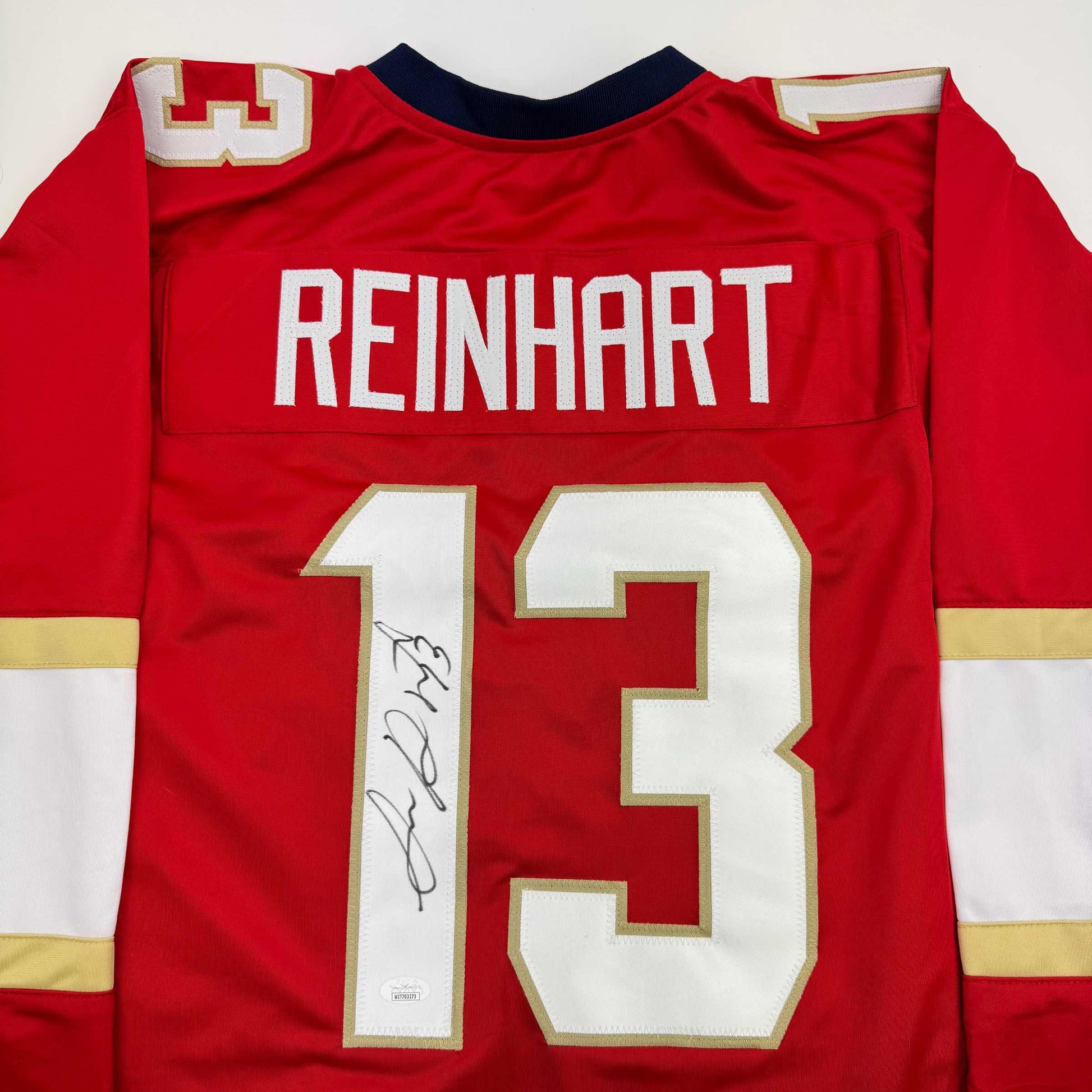 Back view of red hockey jersey displaying "REINHARDT" nameplate and number 13 with handwritten signature on white number panel.