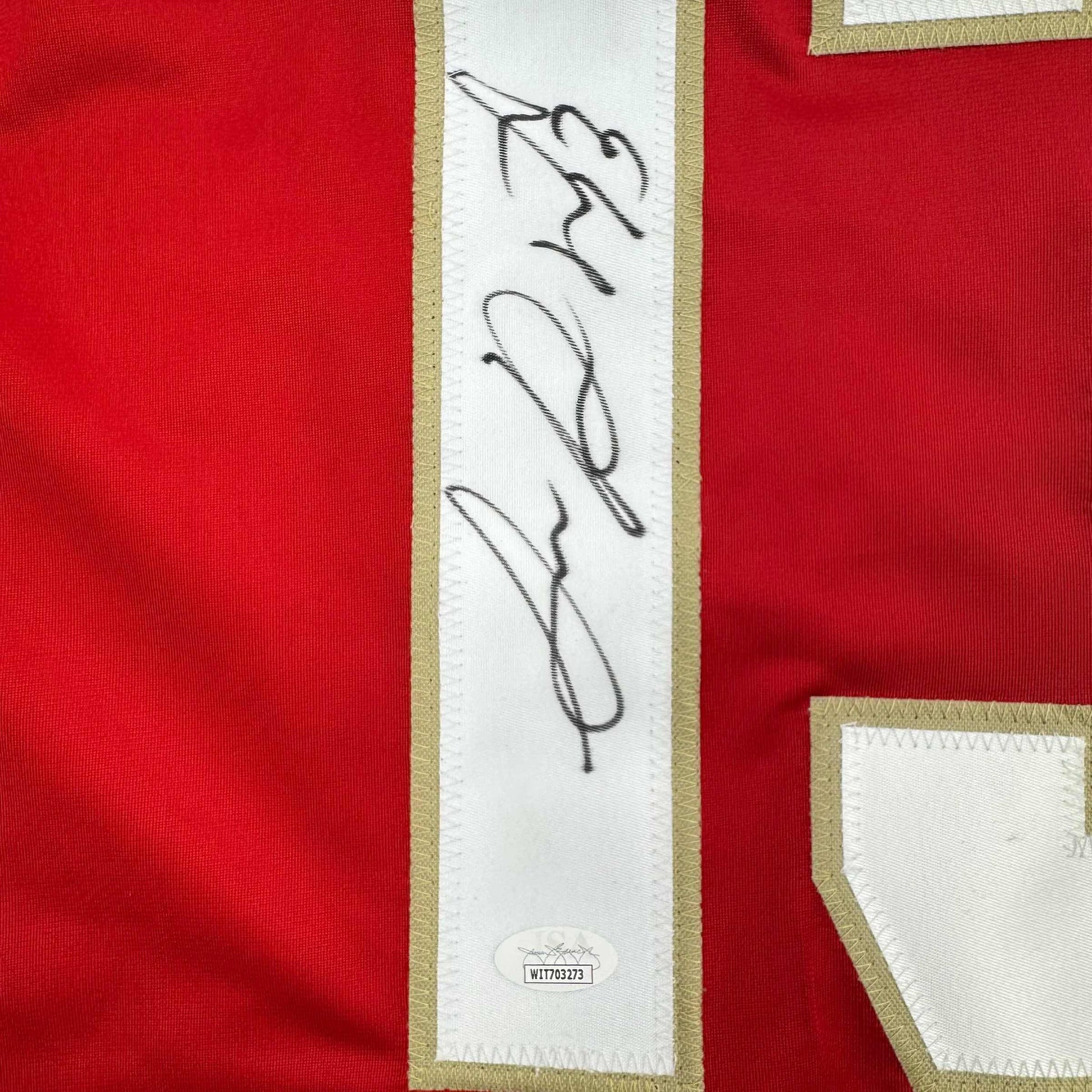 Close-up of signed white stripe on red hockey jersey with black autograph and JSA authentication label visible.