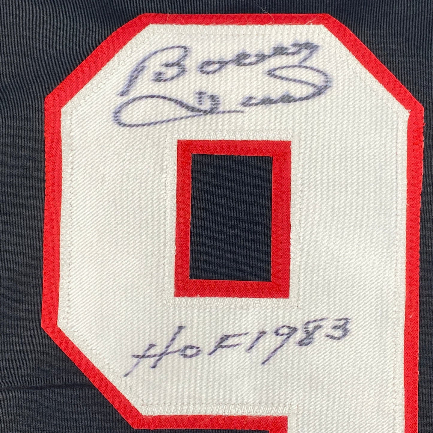 Close-up of signed jersey patch showing autographed number 9 in blue ink on red and white fabric.