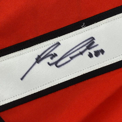 Close-up of white fabric strip with navy handwritten signature on red and black striped hockey jersey.