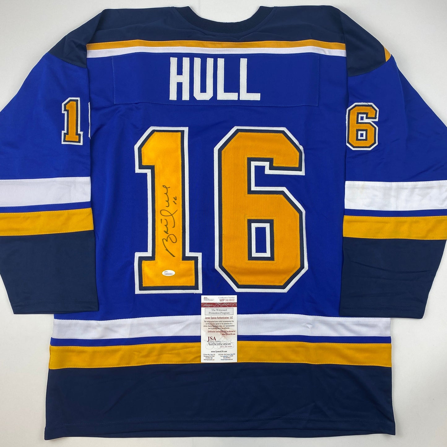 Signed Brett Hull St. Louis Blues jersey displaying number 16 in blue with gold and white trim, flat lay view showing back with JSA authentication certificate.