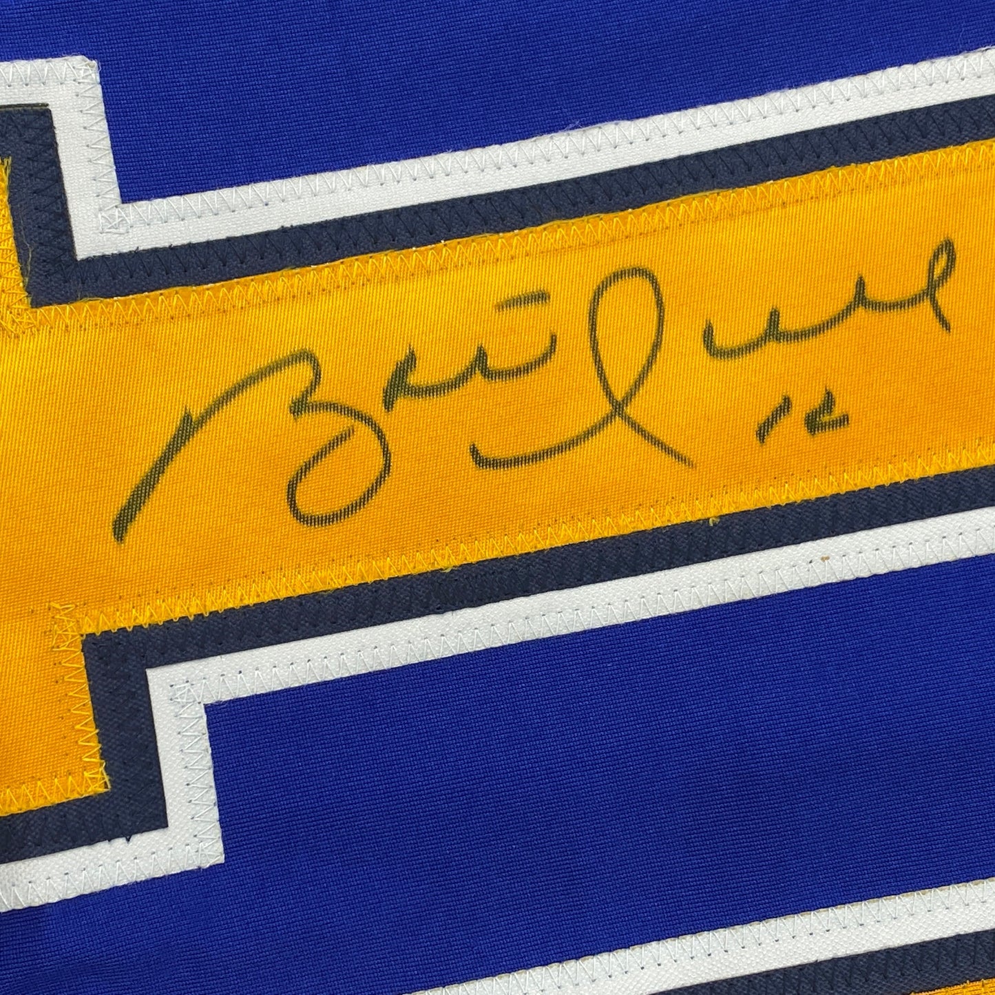 Close-up of handwritten signature on yellow stripe of blue and gold hockey jersey with white and black trim.
