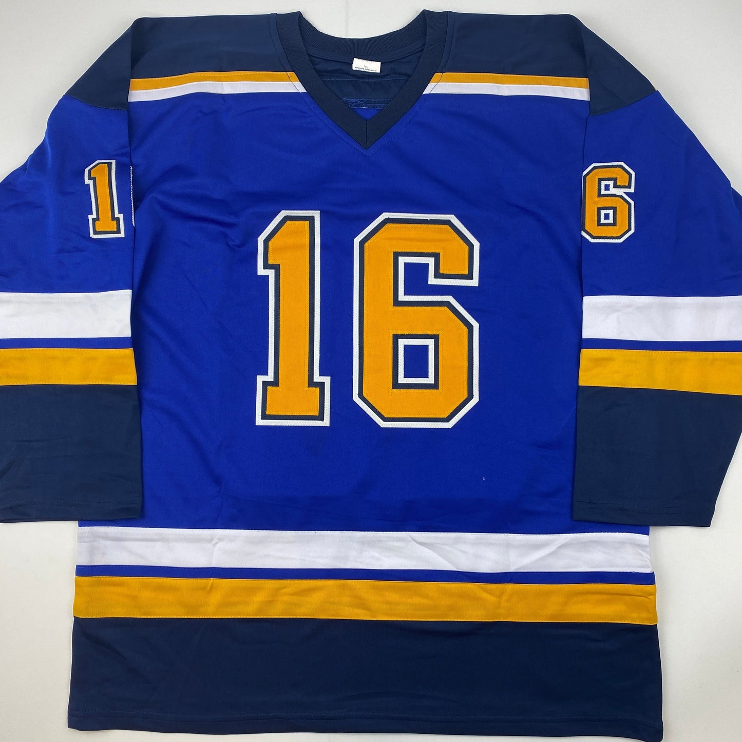 Blue hockey jersey with gold number 16 and navy/gold striped shoulders displayed flat against white background.
