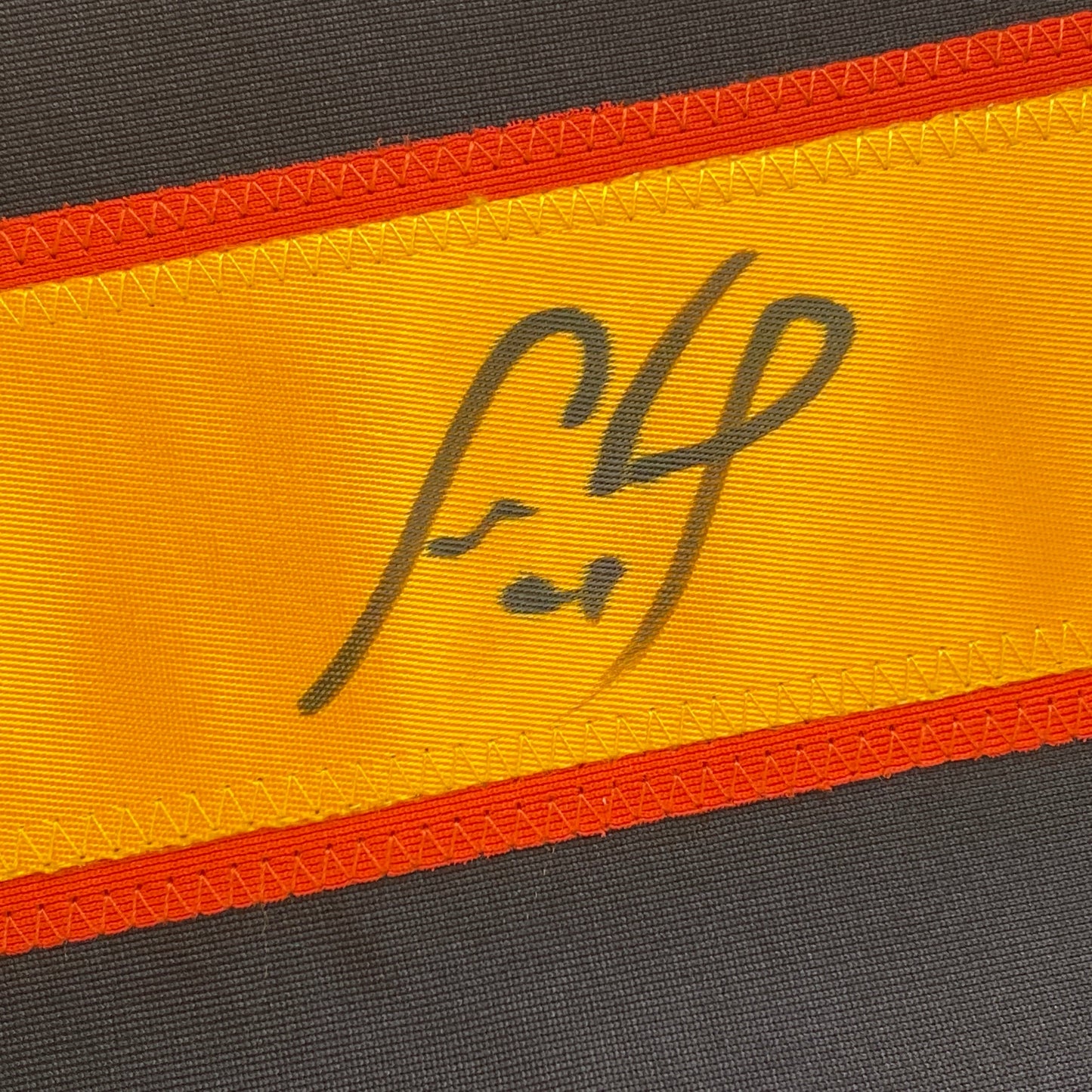 Close-up of yellow and orange striped ribbon with handwritten "42" in dark ink on gray fabric background.