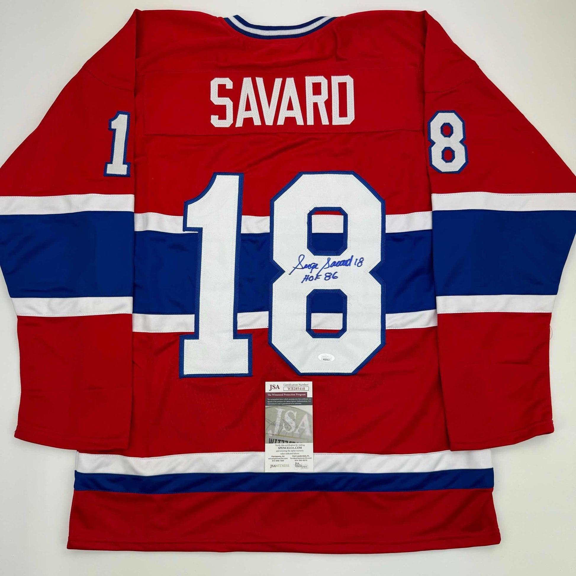 Back view of red, white, and blue Montreal Canadiens hockey jersey number 18 with "SAVARD" nameplate and blue autograph signature with "HOF 86" inscription, JSA authentication certificate visible at bottom.