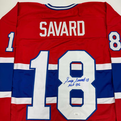 Back view of red, white, and blue Montreal Canadiens hockey jersey with "SAVARD" and number 18 visible, displaying autographed number 18 with "Serge Savard 18 HOF 86" inscription.
