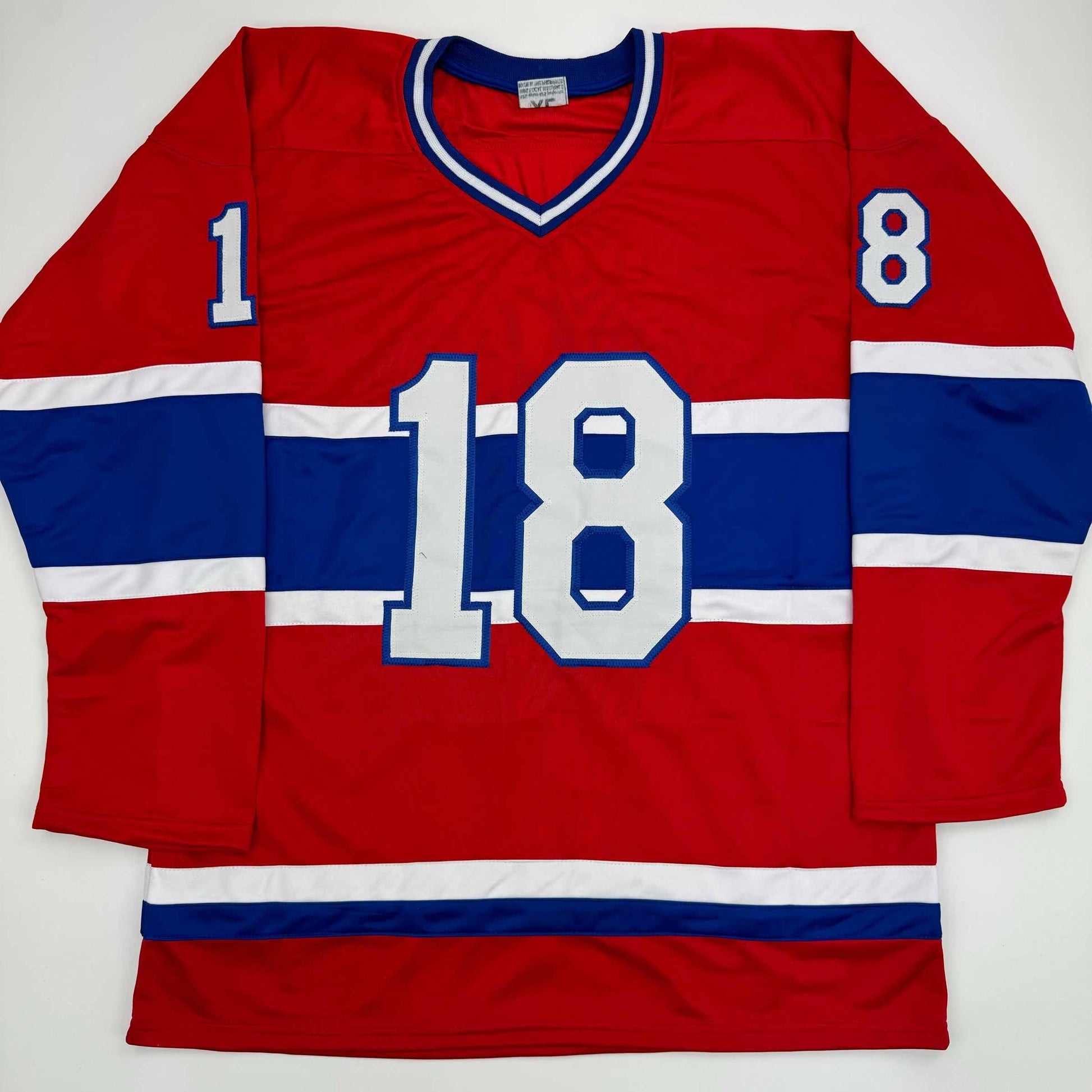 Red and blue Montreal Canadiens hockey jersey number 18 displayed flat against white background, showing front view with white striping and v-neckline.