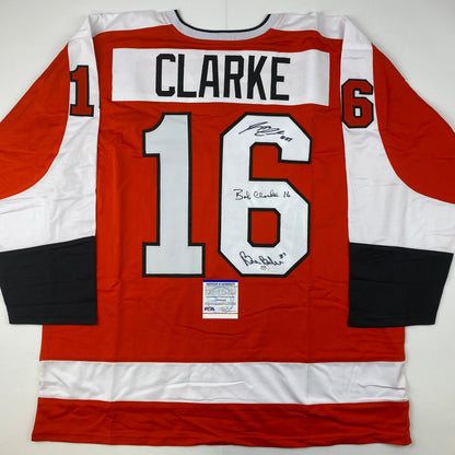 Back view of red and white hockey jersey number 16 with "CLARKE" nameplate and multiple autographs, PSA authentication certificate visible.