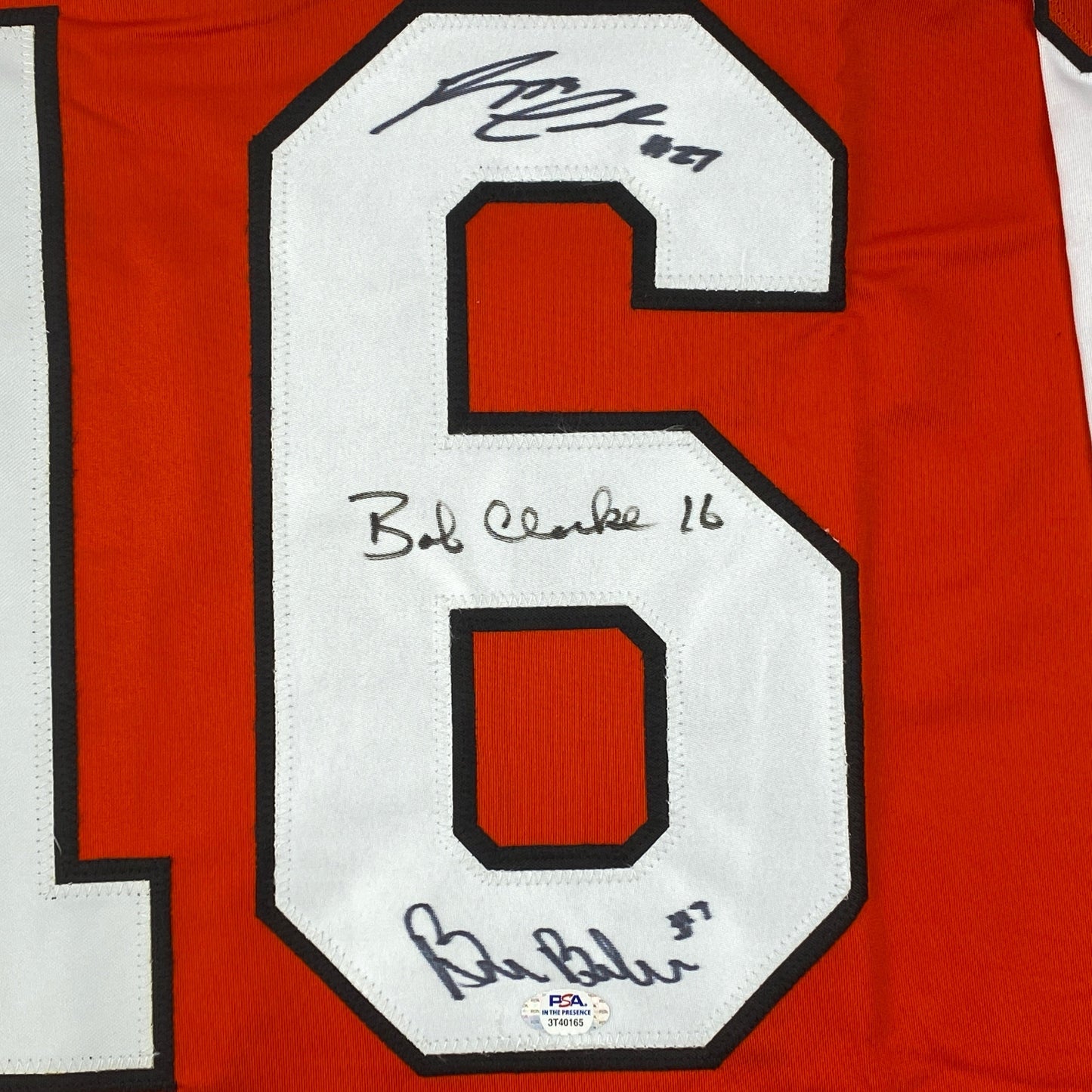 Close-up of number 6 on red jersey with three handwritten signatures and "Bud Clarke 16" notation on white fabric.