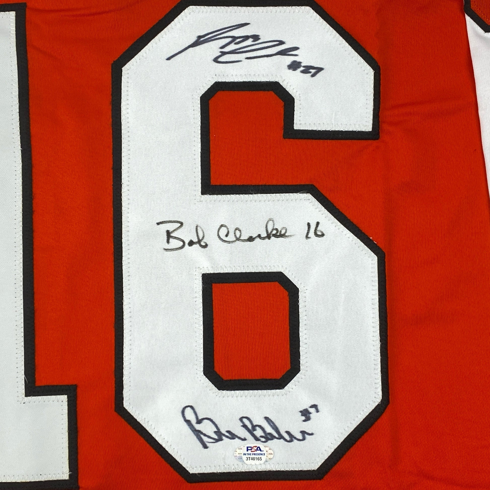 Close-up of number 6 on red jersey with three handwritten signatures and "Bud Clarke 16" notation on white fabric.