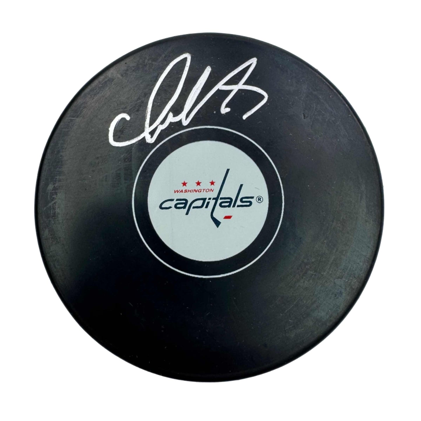 Black hockey puck with white signature and Washington Capitals logo on light circular center label, top-down view.