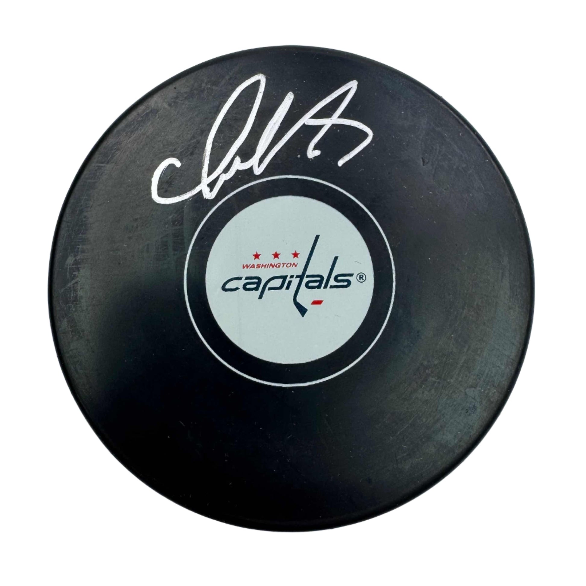Black hockey puck with white signature and Washington Capitals logo on light circular center label, top-down view.