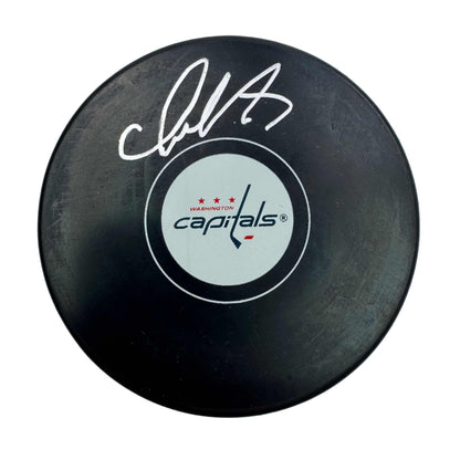 Black hockey puck with white signature and Washington Capitals logo on light circular center label, top-down view.