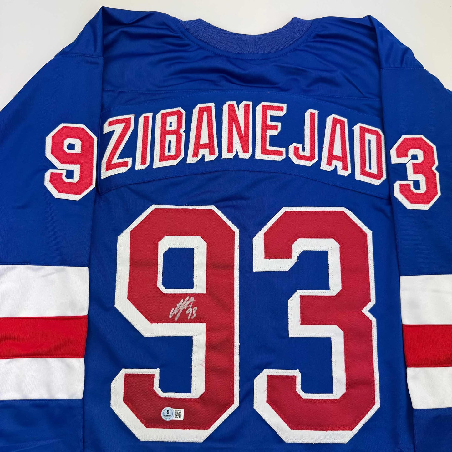 Blue hockey jersey with red and white "ZIBANEJAD 93" lettering and numbers, displayed flat showing front with autograph on number.