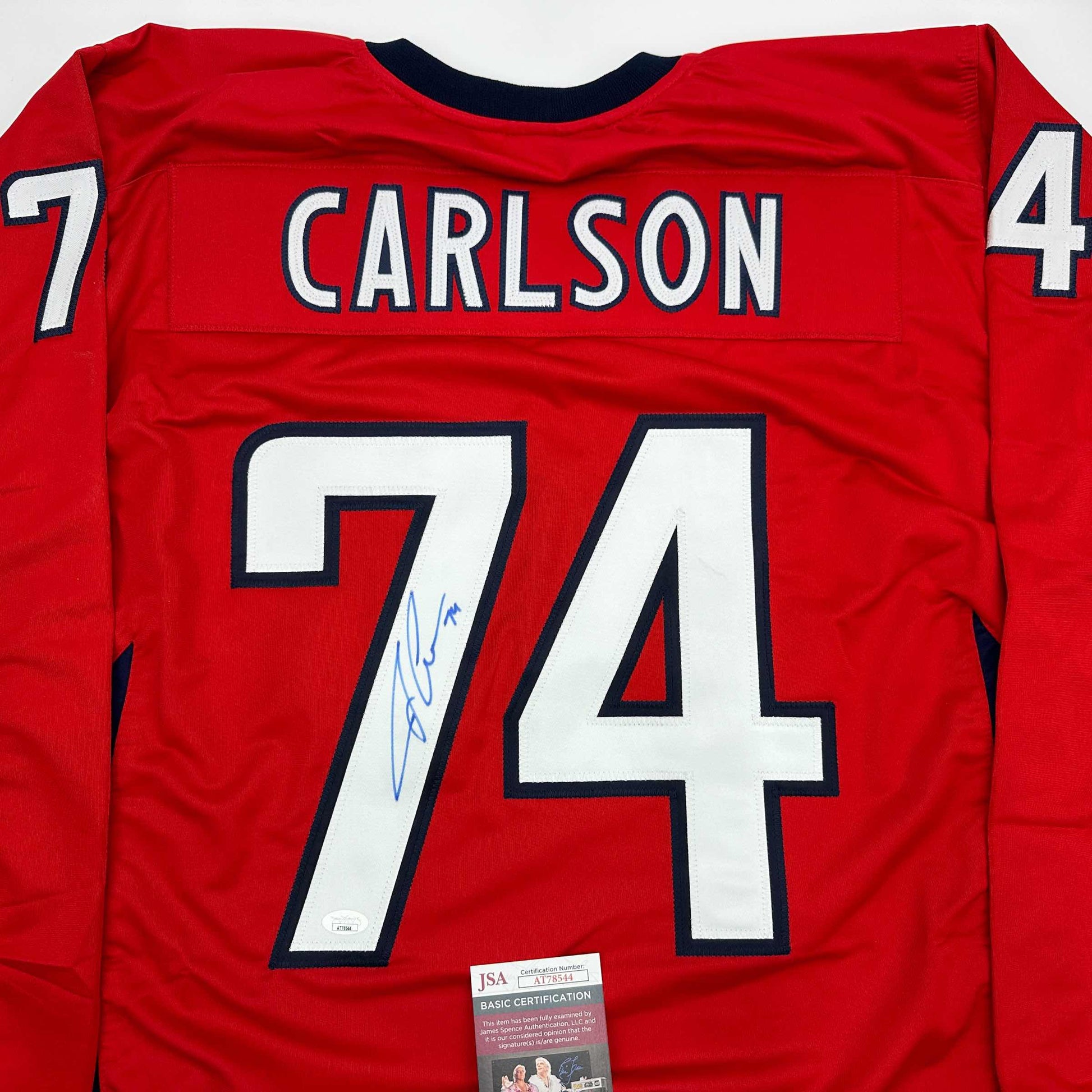 Red hockey jersey back displaying "CARLSON" nameplate and number 74 with blue signature and JSA authentication label.