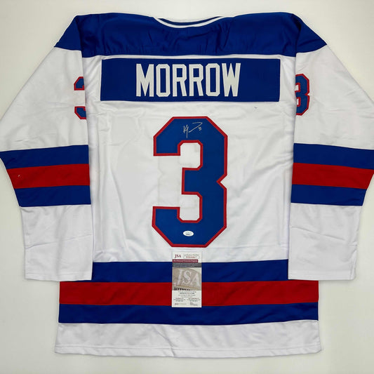 Back view of white hockey jersey with blue and red horizontal stripes, displaying "MORROW" and number 3 with signature and JSA authentication certificate.