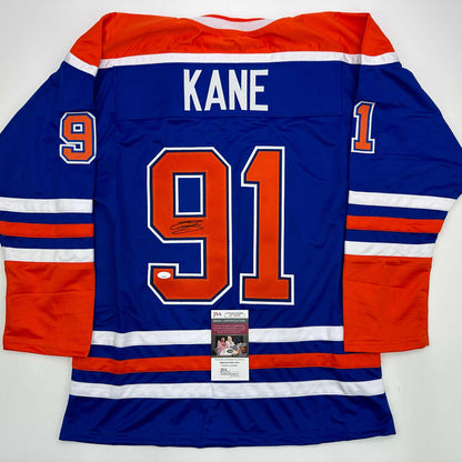 Back view of blue Edmonton Oilers hockey jersey with "KANE 91" in orange and white lettering, JSA authentication certificate visible.