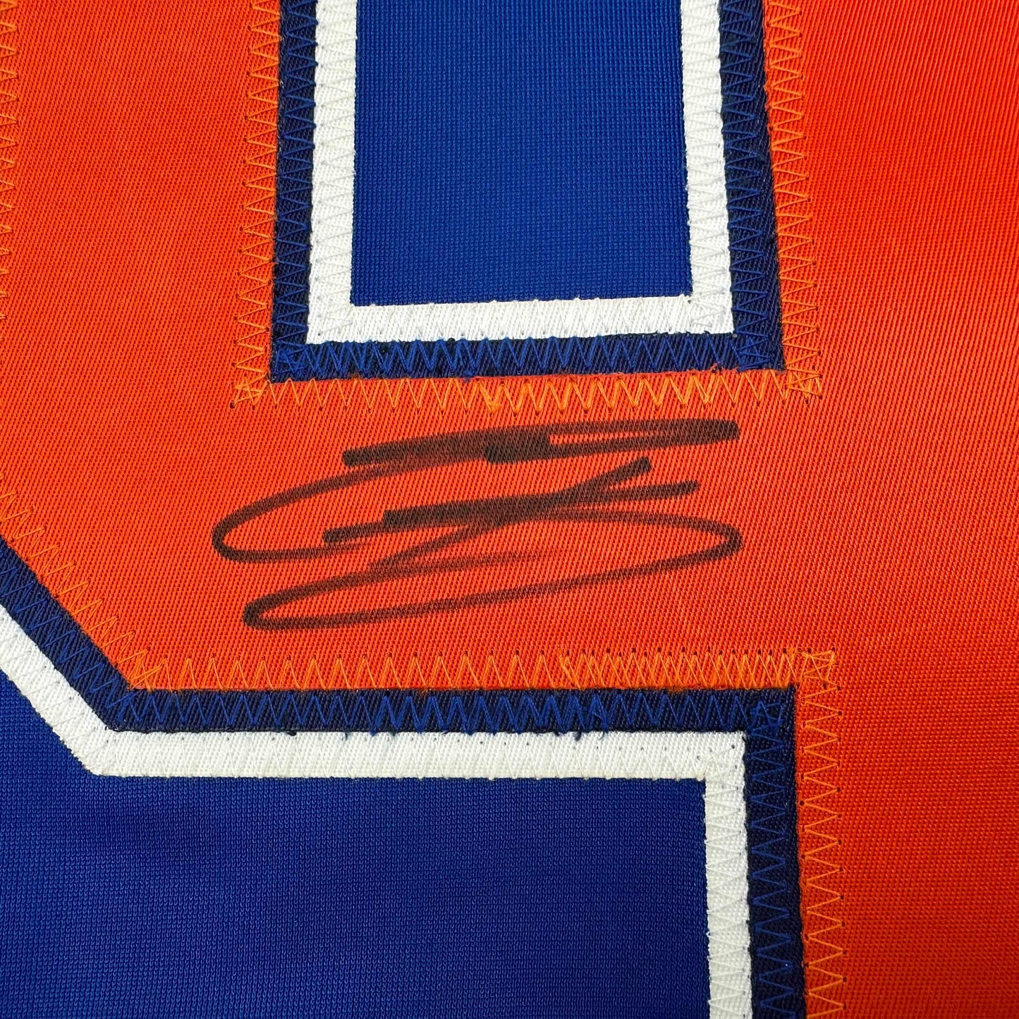 Close-up of signed Edmonton Oilers hockey jersey showing orange and blue panels with handwritten signature in black marker.
