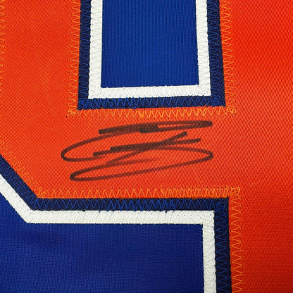 Close-up of signed Edmonton Oilers hockey jersey showing orange and blue panels with handwritten signature in black marker.