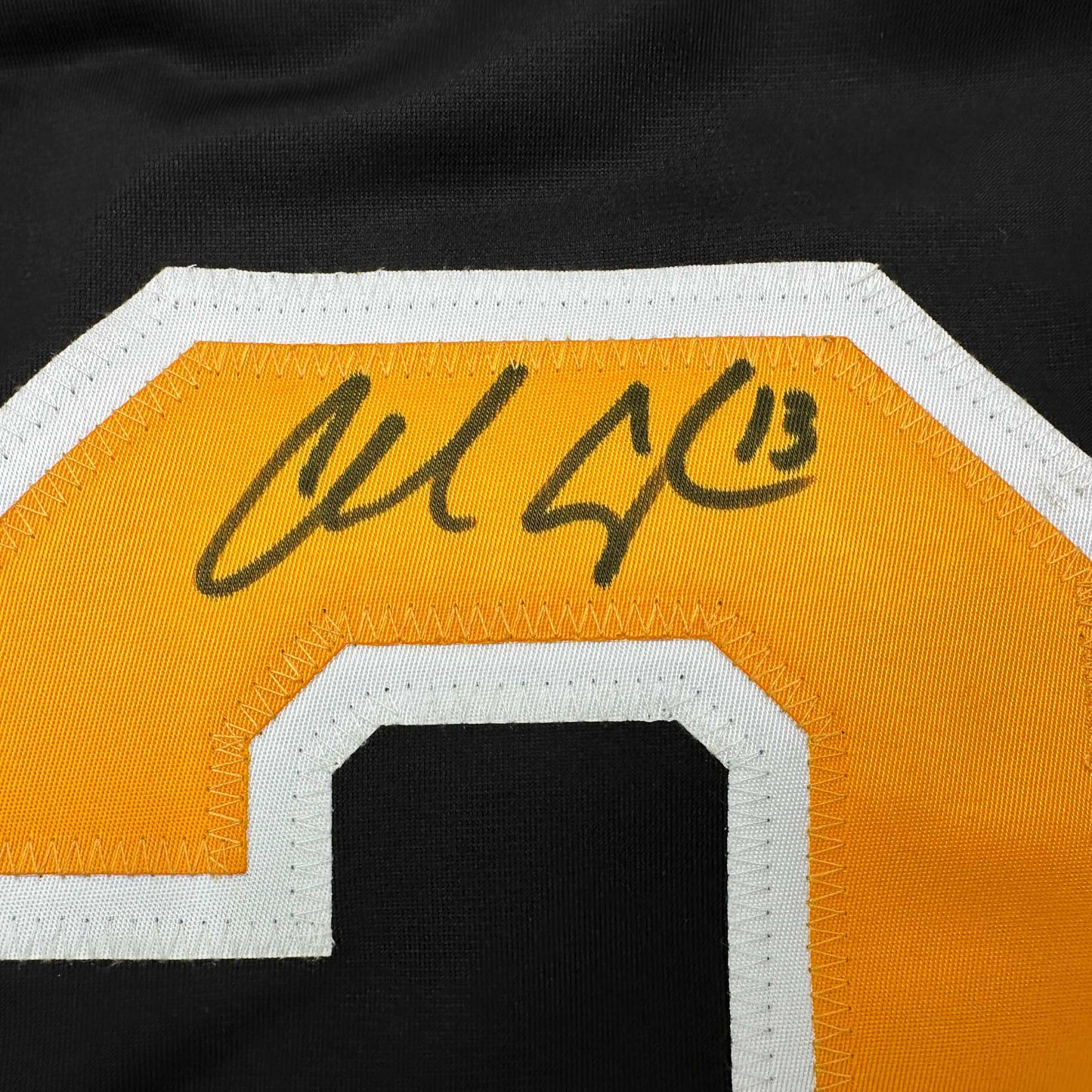 Close-up of autographed gold and white hockey jersey showing handwritten signature on orange fabric with white trim.