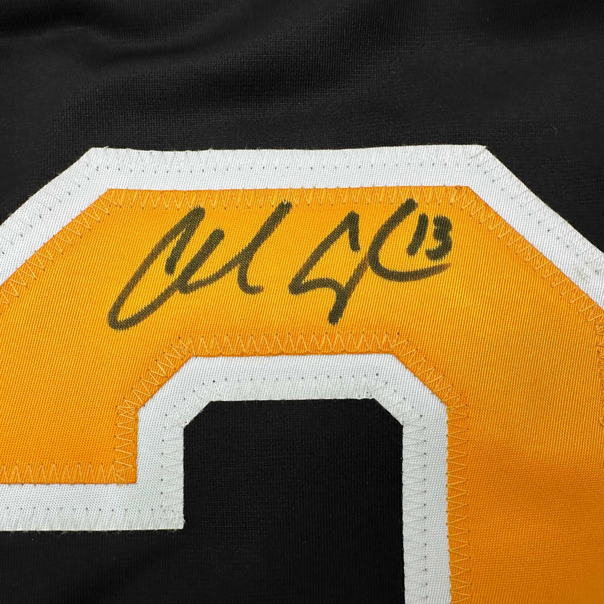 Close-up of autographed gold and white hockey jersey showing handwritten signature on orange fabric with white trim.