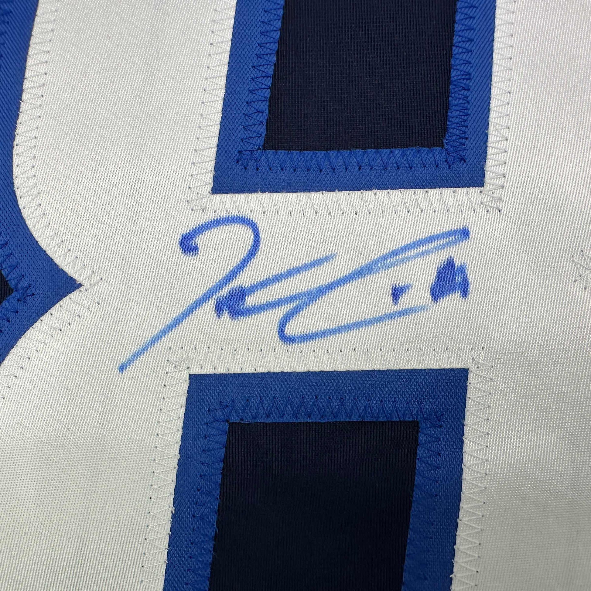 Close-up of blue signature on white jersey fabric with blue and black striped panels visible.
