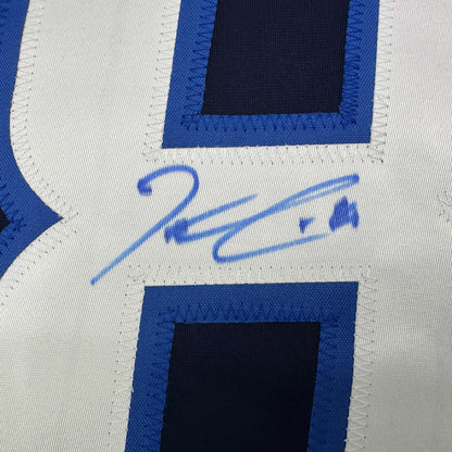 Close-up of blue signature on white jersey fabric with blue and black striped panels visible.