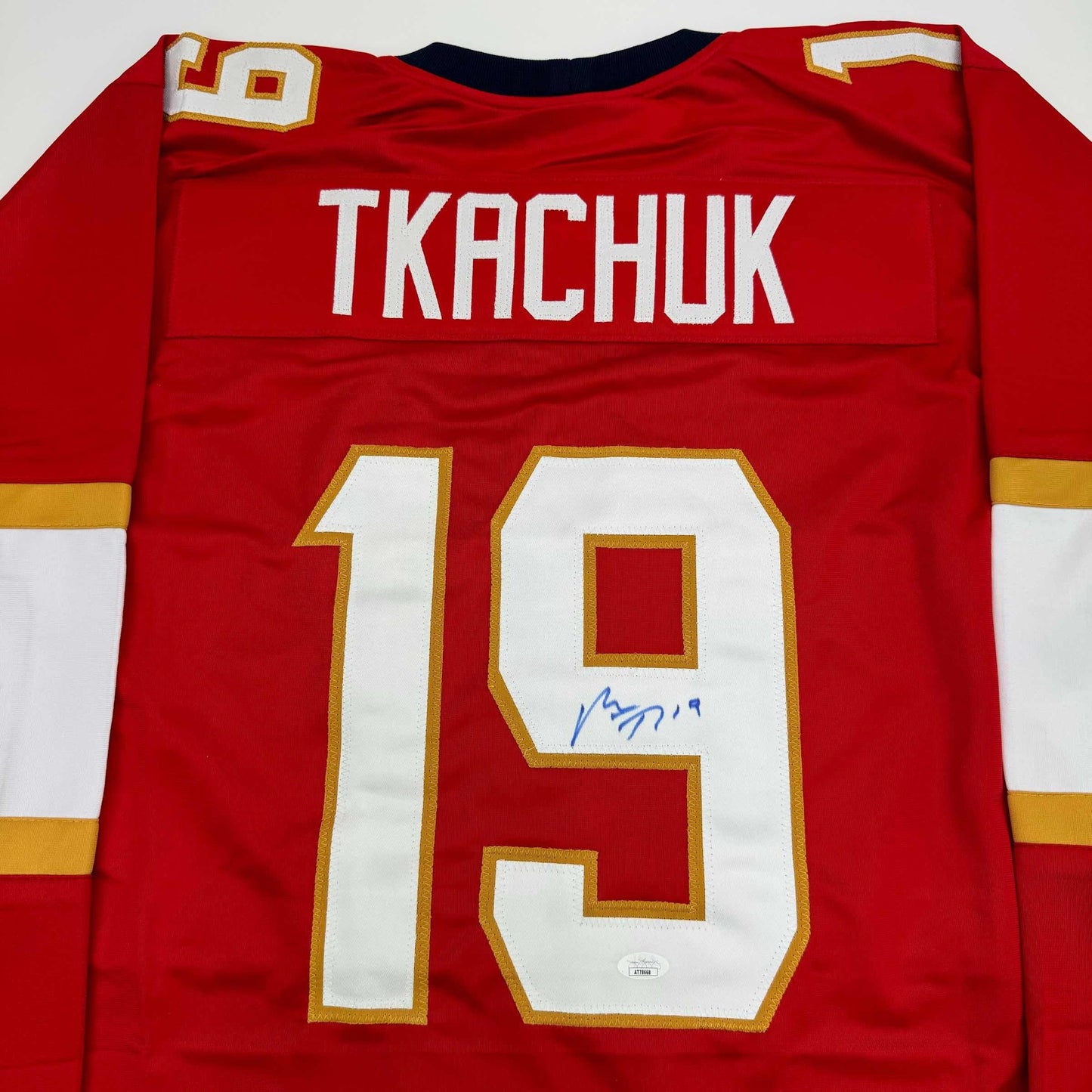 Red hockey jersey displaying "TKACHUK" and number 19 with gold and white trim, signed in blue ink.