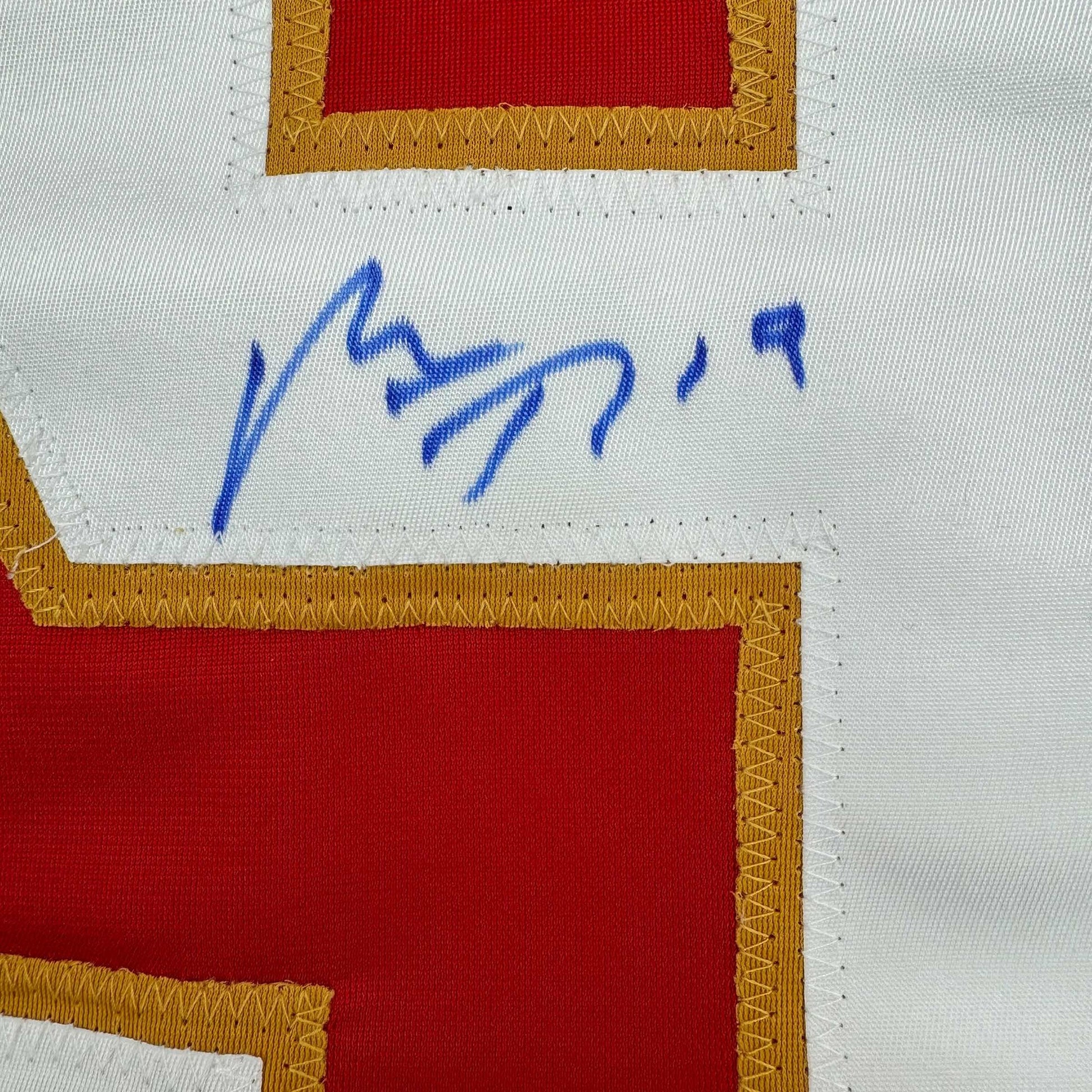 Close-up of blue autograph signature on white jersey label with red and gold trim visible.