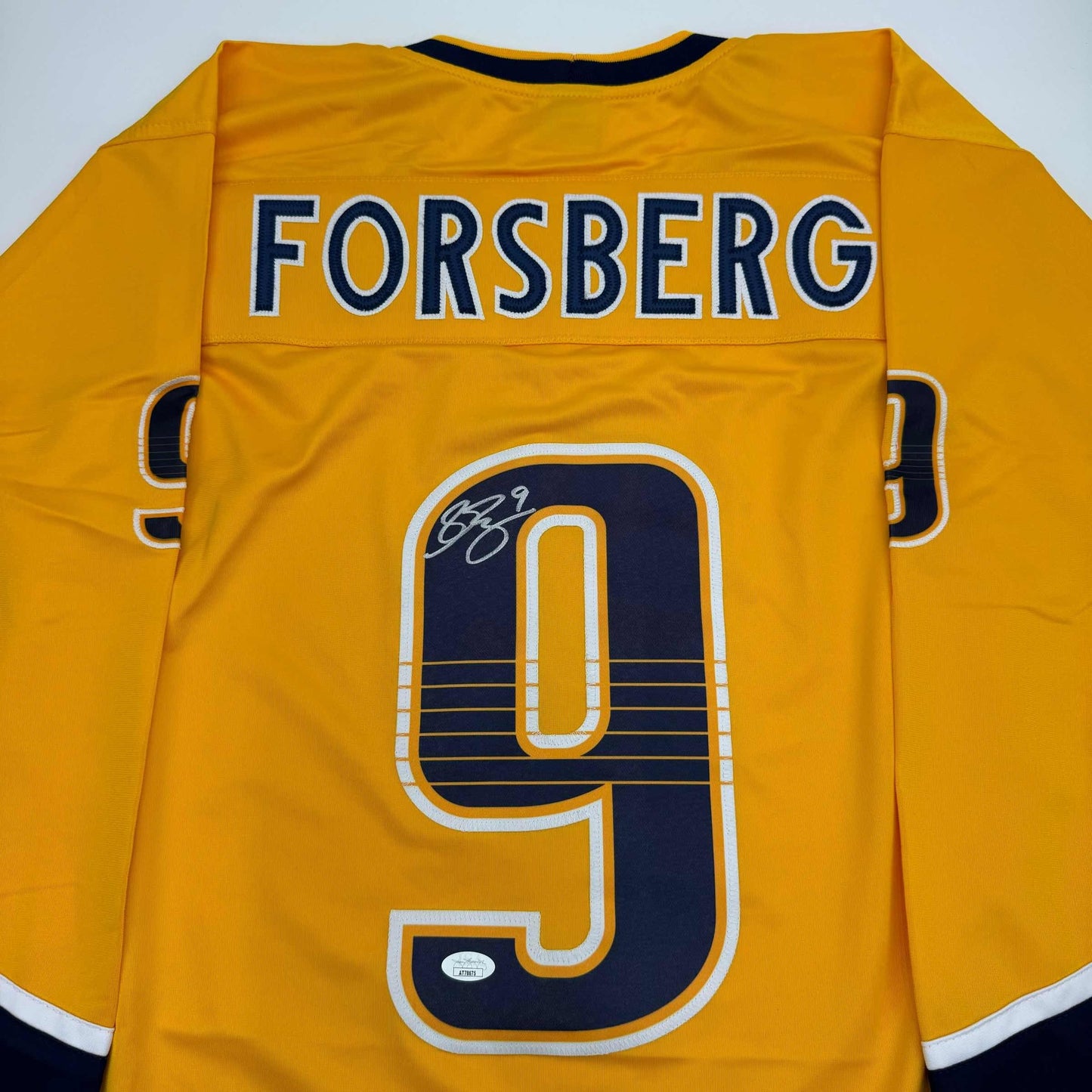 Back view of yellow hockey jersey with "FORSBERG" and number 9 in navy and white, with signature on navy number.